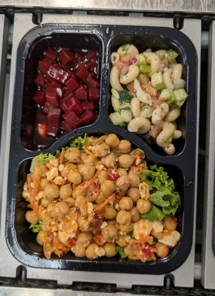 La imagen muestra una comida a domicilio preparada en nuestra cocina: ensalada griega de garbanzos, ensalada de pasta y remolacha encurtida.